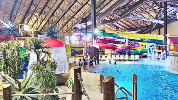 An indoor water park with a large pool, multiple water slides, and artificial palm trees. - Cranmore Ski Retreat • Arcade + Firepit + Dogs OK! (Conway)