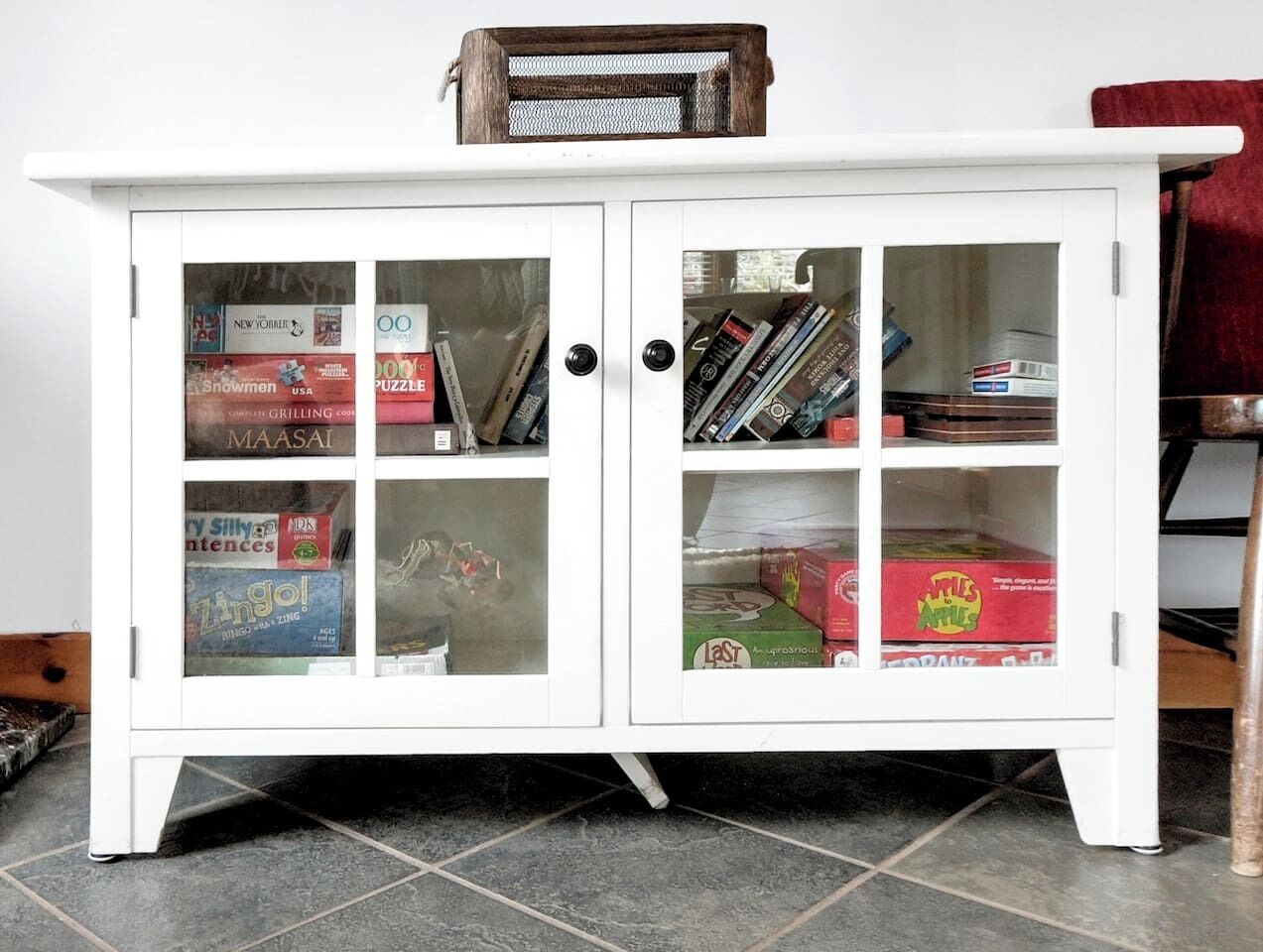 A white cabinet with glass doors containing various items like books, magazines, and boxes.