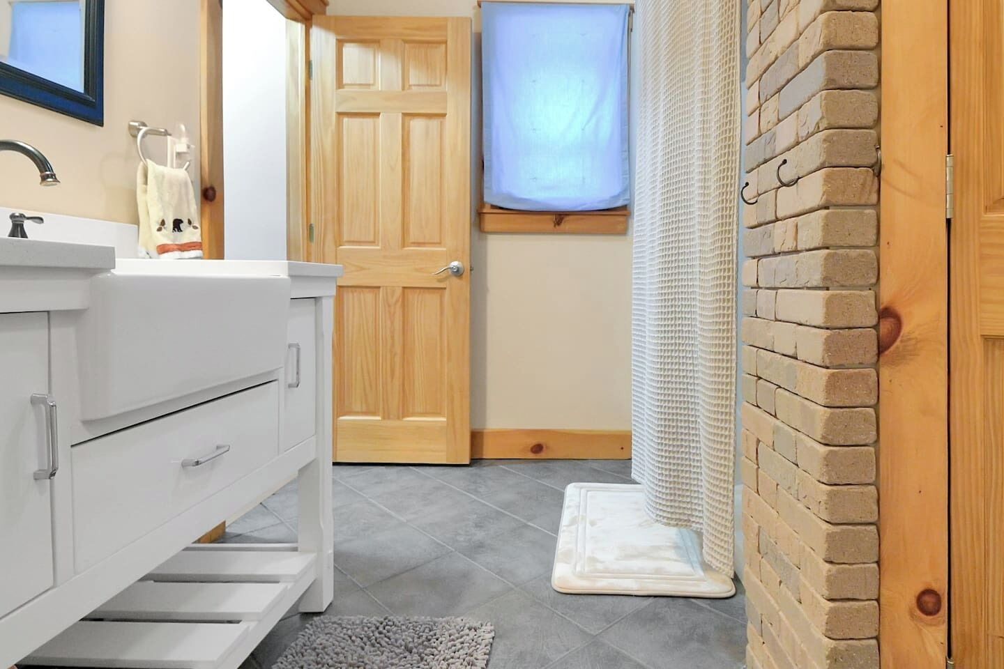 Een badkamer met een wit wastafelmeubel, een houten deur, een douchegordijn en een betegelde vloer.