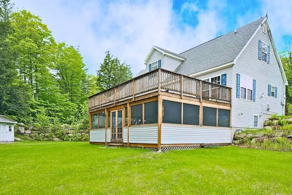 A two-story house with a balcony, a covered porch, and a stone wall in the background.