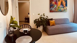 Una sala de estar con una mesa redonda, sillas, un sofá, un cuadro y una planta en maceta.