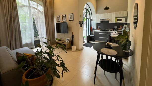Una sala moderna con un sofá, una mesa de comedor con sillas, un televisor y una zona de cocina con un microondas y armarios.