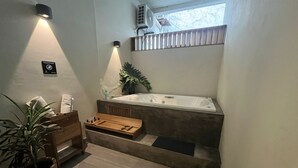 Un baño moderno con una bañera grande, un banco de madera, una planta en maceta y un equipo de aire acondicionado instalado en la pared.