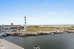 Un faro en un muelle, con un estacionamiento y vistas del horizonte urbano.