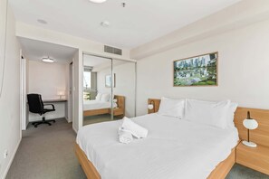 A hotel room with a bed, a desk, a chair, a lamp, and a painting on the wall.