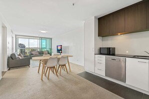 A modern apartment with a dining area, kitchen, and a large window offering a city view.