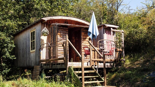 Une cabane en bois rustique, dotée d’une véranda, de quelques marches et d’un petit espace extérieur aménagé pour s’asseoir.