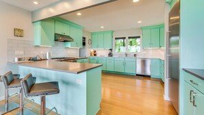 A modern kitchen with teal cabinets, a stainless steel refrigerator, and a central island with bar stools. - Mtn-View Home w/ Pickleball Court in Louisville! (Louisville)