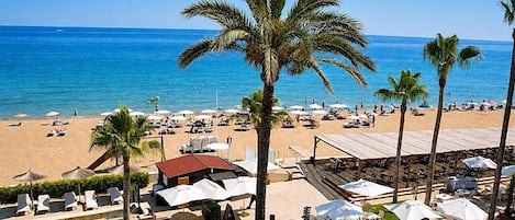 A beach resort with sun loungers, umbrellas, and palm trees.