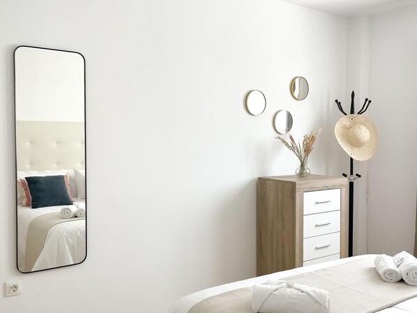 Una habitación de hotel con un espejo grande, un aparador de madera, un perchero para sombreros y camas bien hechas.