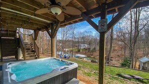 Un jacuzzi debajo de una terraza de madera con vista a un jardín trasero y casas.