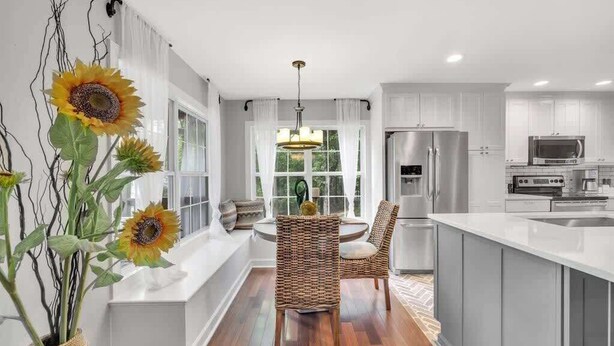 Una cocina moderna con armarios blancos, una isla central y una zona de comedor con sillas de mimbre.
