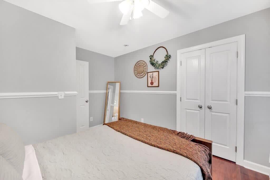 A bedroom with a bed, white walls, a ceiling fan, and a door.