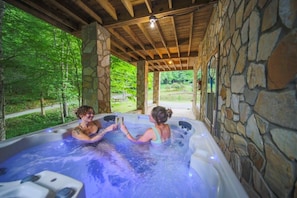 A hot tub area with stone walls and wooden beams, surrounded by greenery. - Sleeps 16 • Hot Tub•Sauna•Dogs Welcome•Ping Pong (Mars Hill)