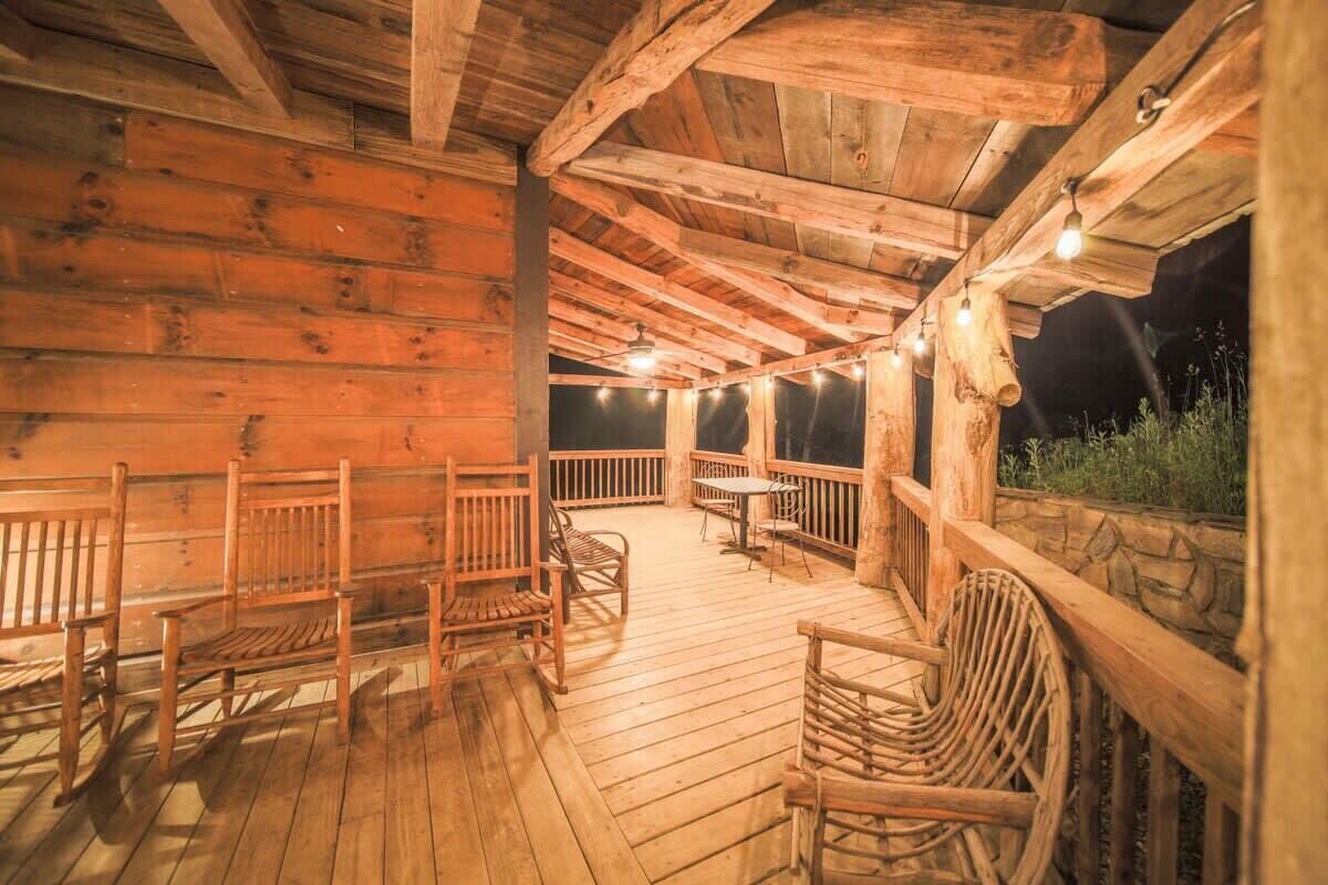 Une cabane en bois dotée d’une terrasse en bois, aménagée avec des chaises et une table en bois, et décorée de guirlandes lumineuses.