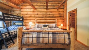 Un dormitorio tipo cabaña de madera con una cama de madera, una cama nido y una colcha escocesa.