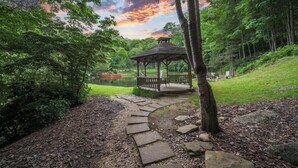 Ein Pavillon in einem Park mit einem Kiesweg, umgeben von Bäumen und einem See.