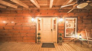 Ein Interieur einer Blockhütte mit einer Holztür, zwei Wandleuchtern, einem kleinen Tisch mit einem Leuchter und einem Stuhl.