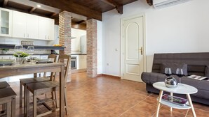 A modern kitchen with white cabinets, a brick column, and a dining area with wooden furniture.