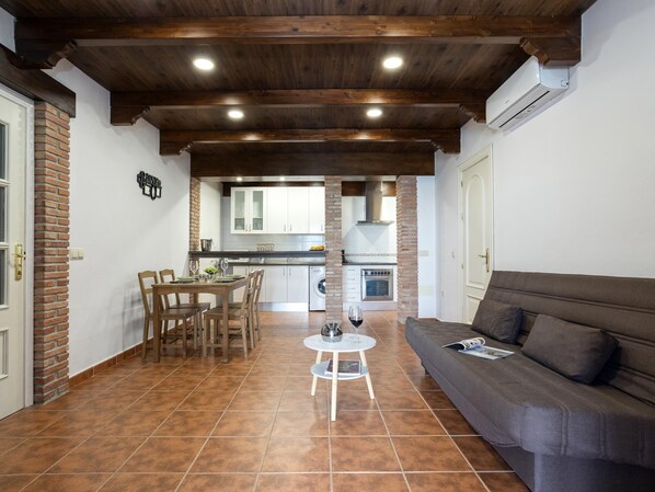 A cozy living area with a sofa, a dining table with chairs, and a kitchen in the background.