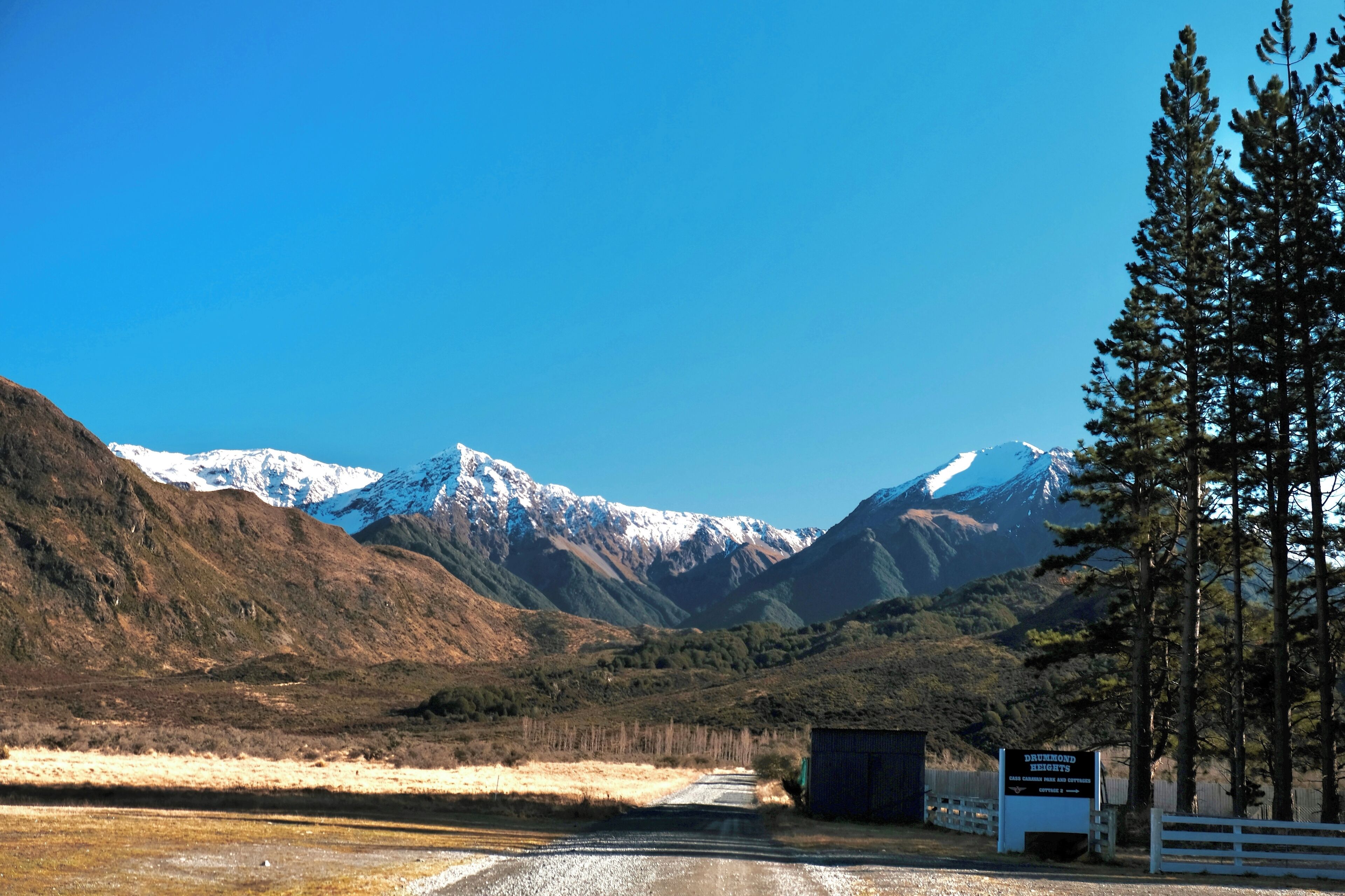 Une route menant à un panneau indiquant l’accès à Drummond Heights, avec une vue sur des montagnes aux sommets enneigés.