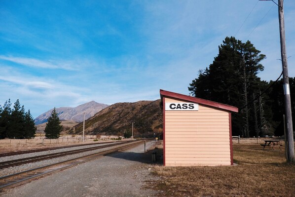 Una pequeña cabaña de madera con la inscripción 'CASS', y un camino de grava que conduce a unas vías de tren.