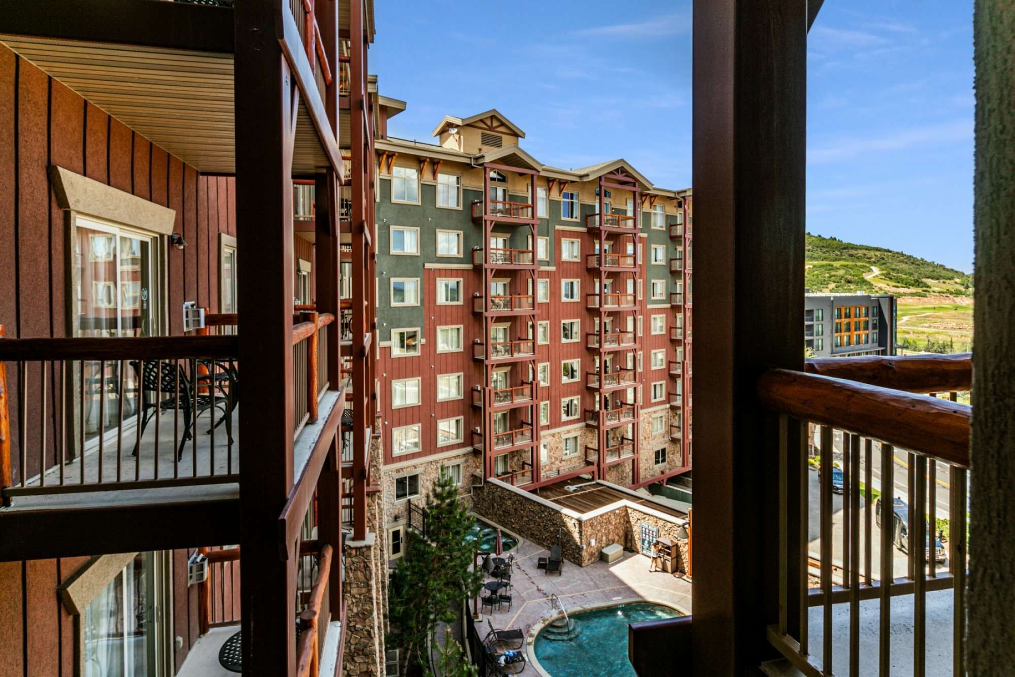 A multi-story hotel with balconies, a swimming pool, and a view of a hilly landscape.