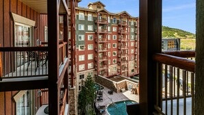 A multi-story hotel with balconies, a swimming pool, and a view of a hilly landscape.