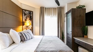 A hotel room with a bed, a desk, a TV, and a window with curtains.
