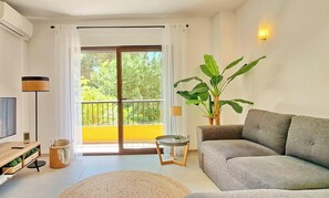 A living room with a sofa, a TV, a plant, and a balcony with yellow walls.