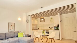 Un appartement moderne avec un canapé gris, une table à manger avec des chaises, une cuisine avec des meubles blancs et une grande plante.