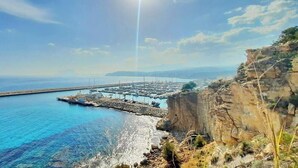 Un port de plaisance sur la côte, avec des bateaux amarrés, une jetée s’avançant dans l’eau et une falaise rocheuse au premier plan.