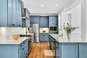 A modern kitchen with blue cabinets, stainless steel appliances, and a white countertop.