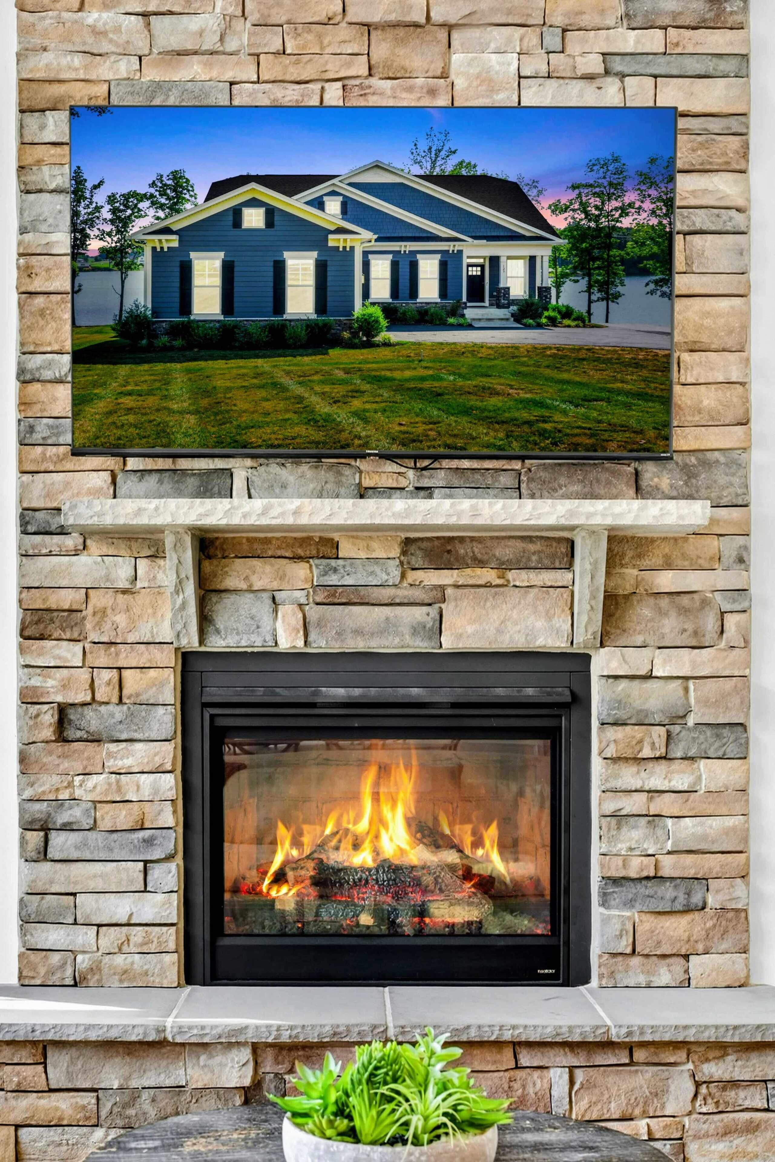 A stone fireplace with a fire, a mounted television displaying a house, and a potted plant.
