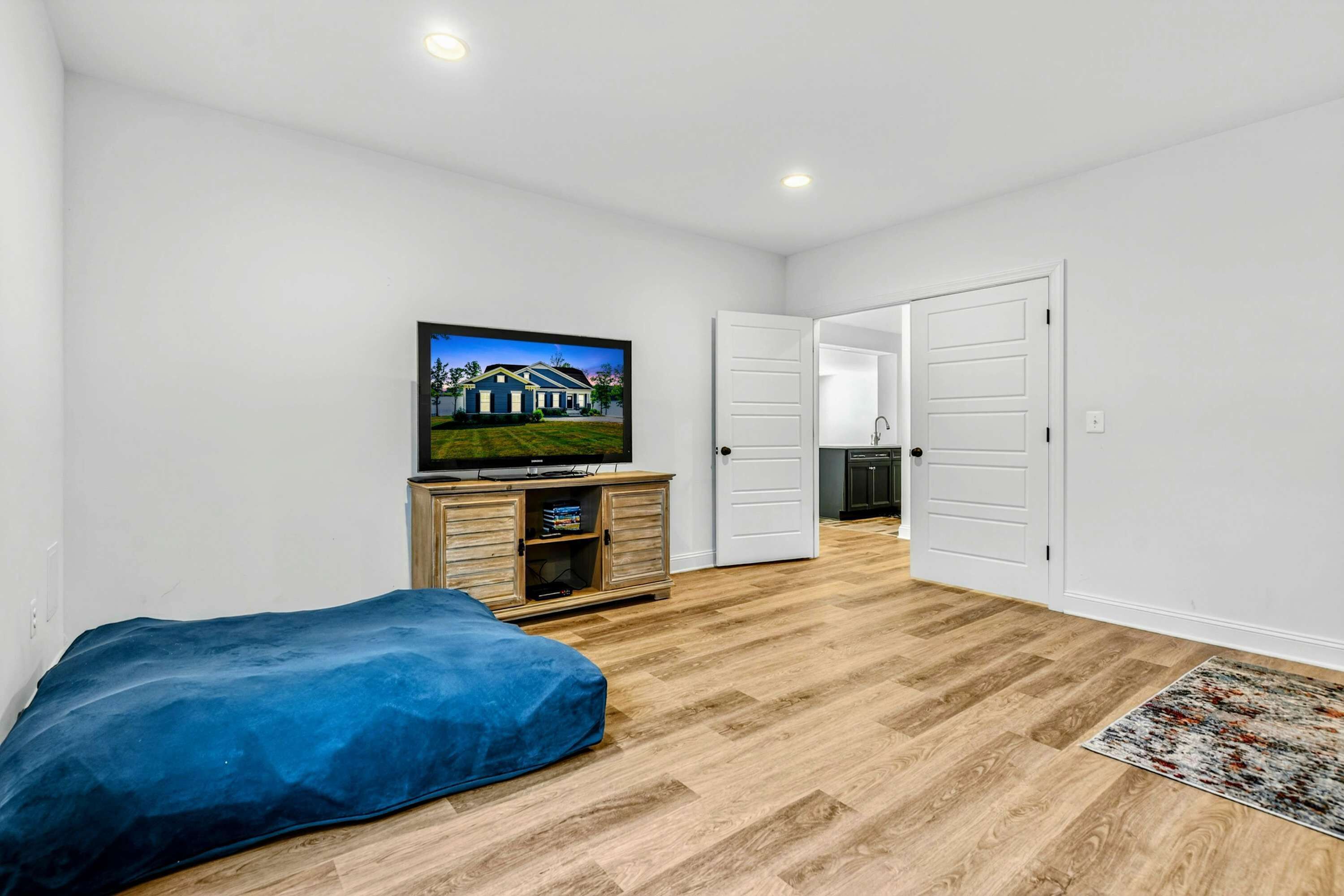 A bedroom with a bed, a television on a wooden cabinet, and a door leading to another room.