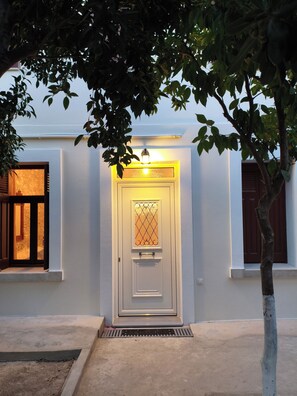 Une maison blanche avec une porte d’entrée, une fenêtre et un arbre au premier plan.