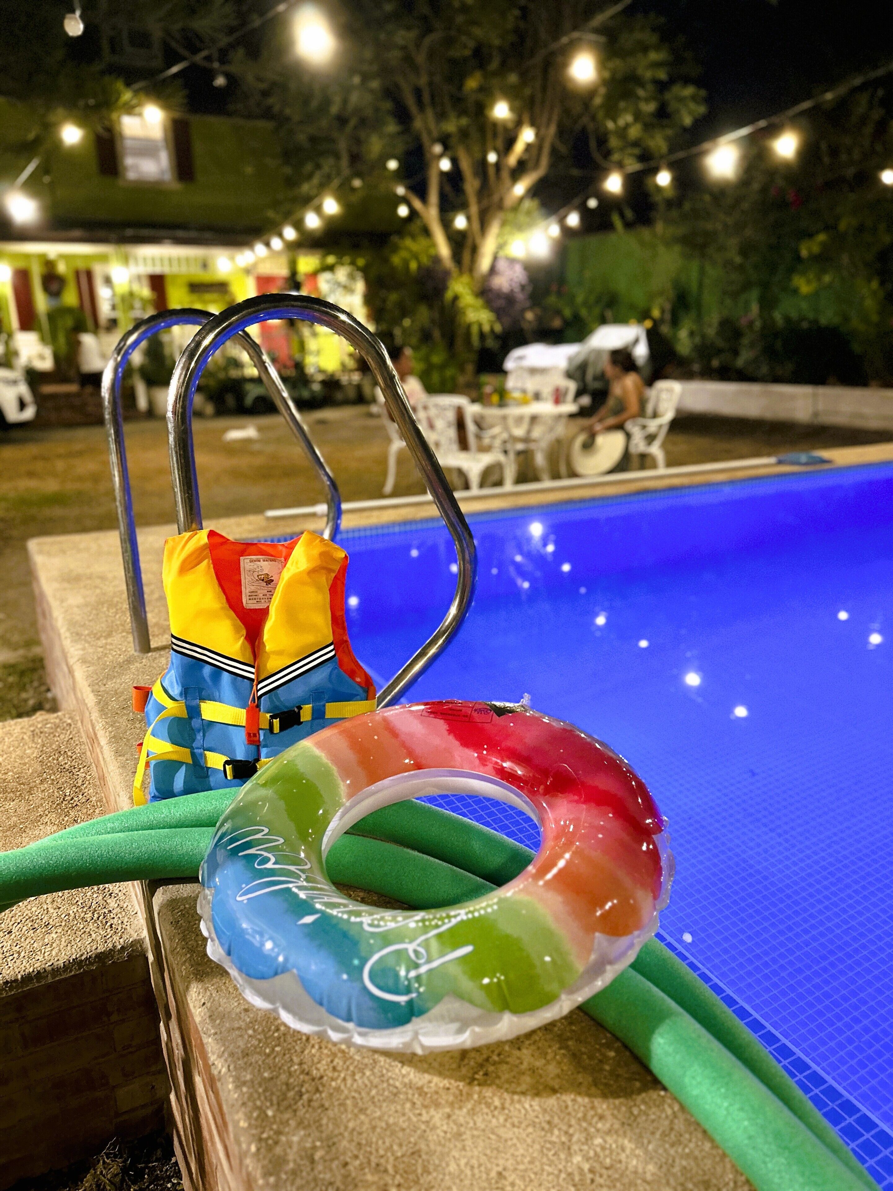 A swimming pool with a blue water surface, a metal pool ladder, and two colorful inflatable rings.