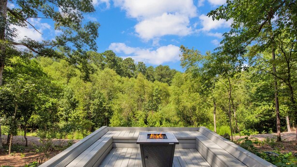 A wooden deck with a built-in fire feature surrounded by lush greenery. - Sweetbay Retreat — Minutes from Fort Bragg, Methodist University, and Downtown! (Fayetteville)