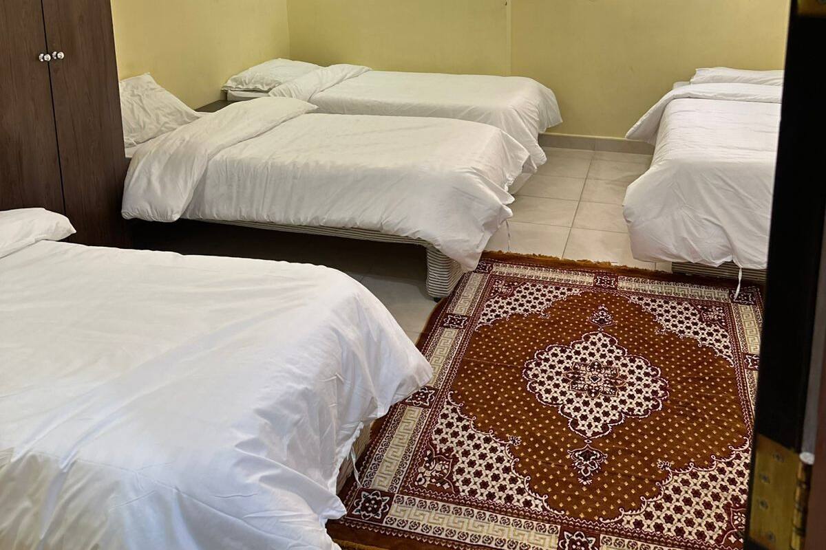 Ein Hotelzimmer mit vier Einzelbetten, einem braunen Teppich mit Muster, einem Fenster mit Blick und einem Holzschrank.