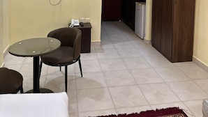 Une chambre d’hôtel avec un téléviseur fixé au mur, une petite table avec des chaises, une armoire et un coin cuisine visible à travers une porte ouverte.