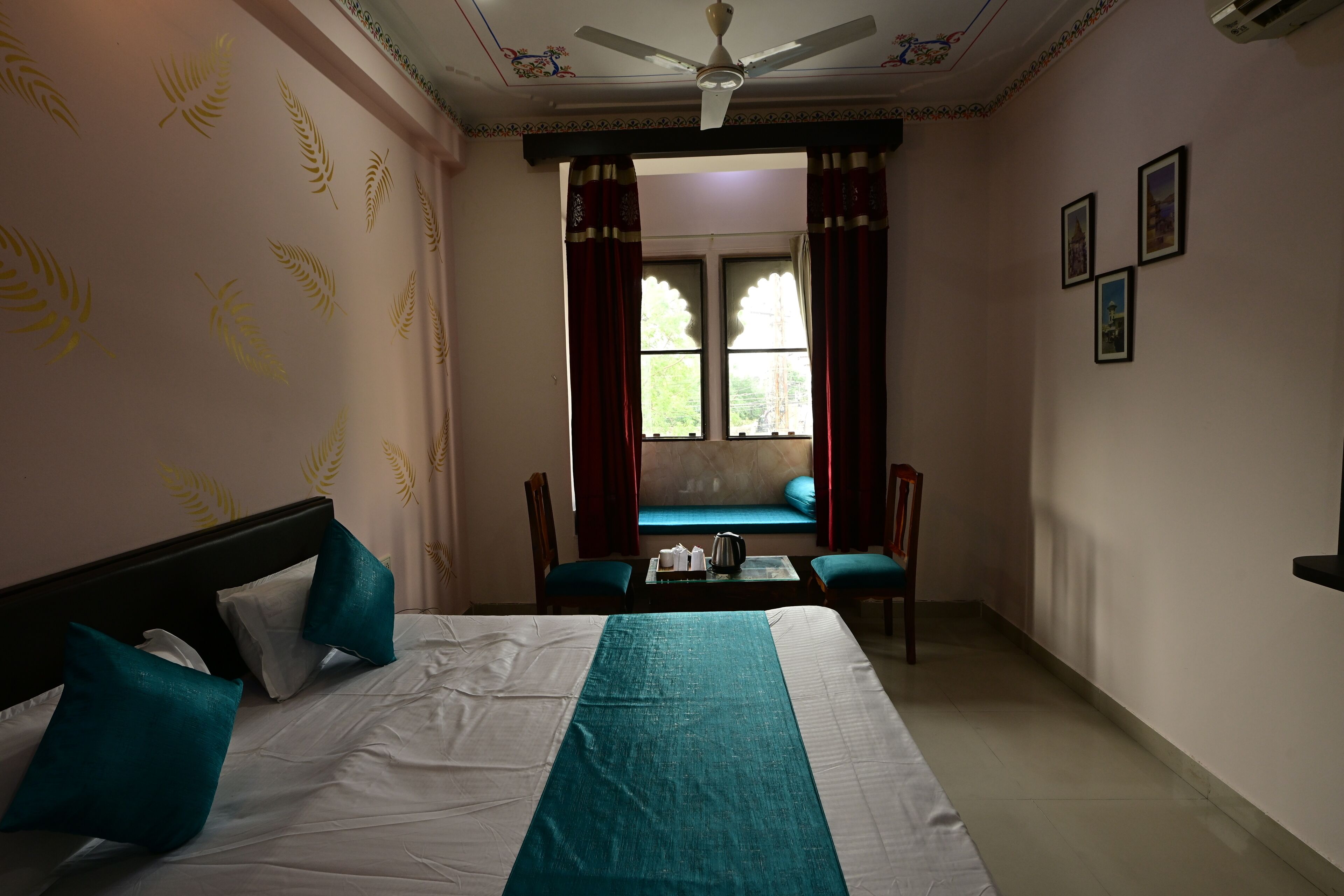 A hotel room with a bed, a table with a kettle, chairs, and a window with curtains.