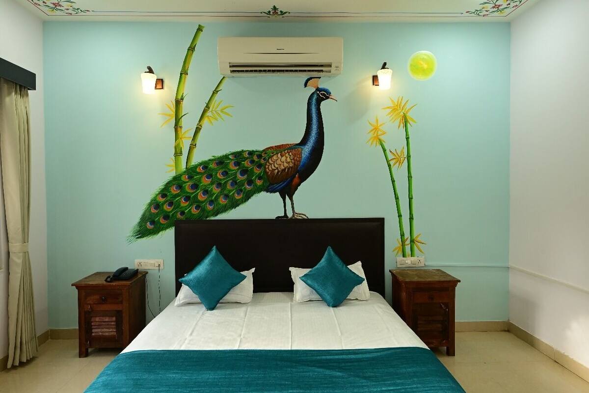 A bedroom with a bed, two nightstands, a peacock mural, an air conditioner, and wall-mounted lights.