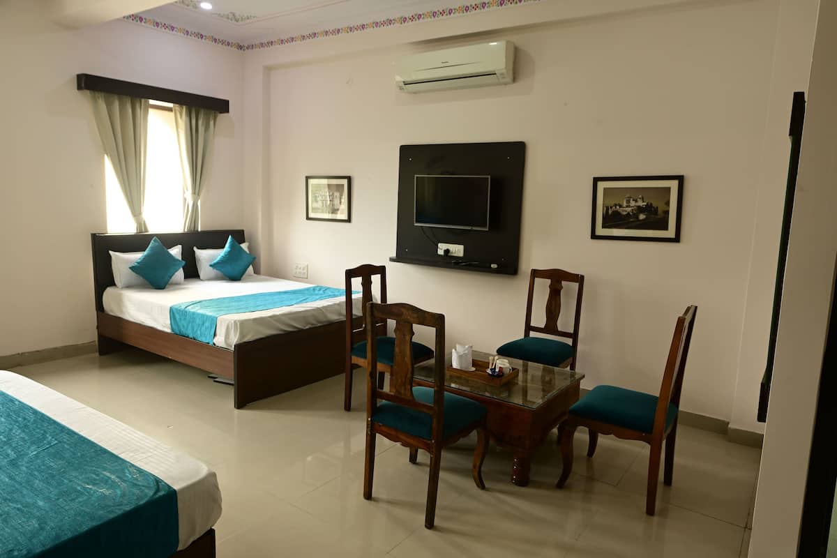 A hotel room with a bed, a TV, a dining table with chairs, and two framed pictures on the wall.