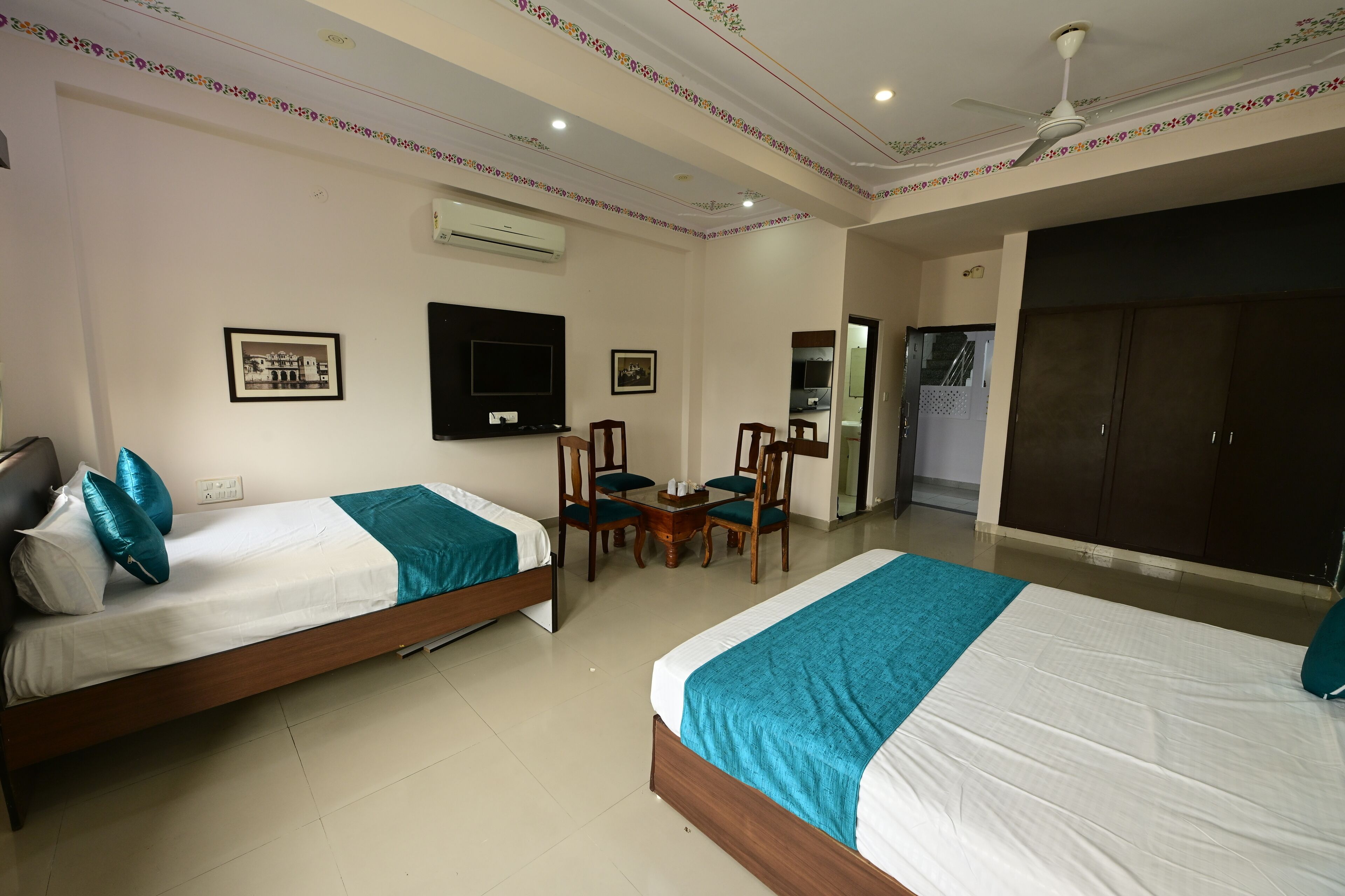 A hotel room with two single beds, a TV, a small table with chairs, and a wardrobe.