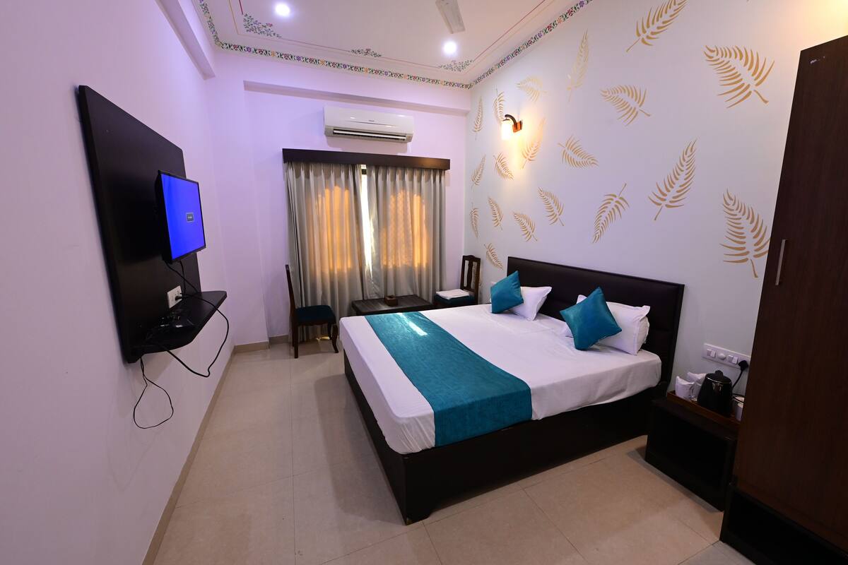 A hotel room with a bed, a TV mounted on the wall, a desk, and a chair.