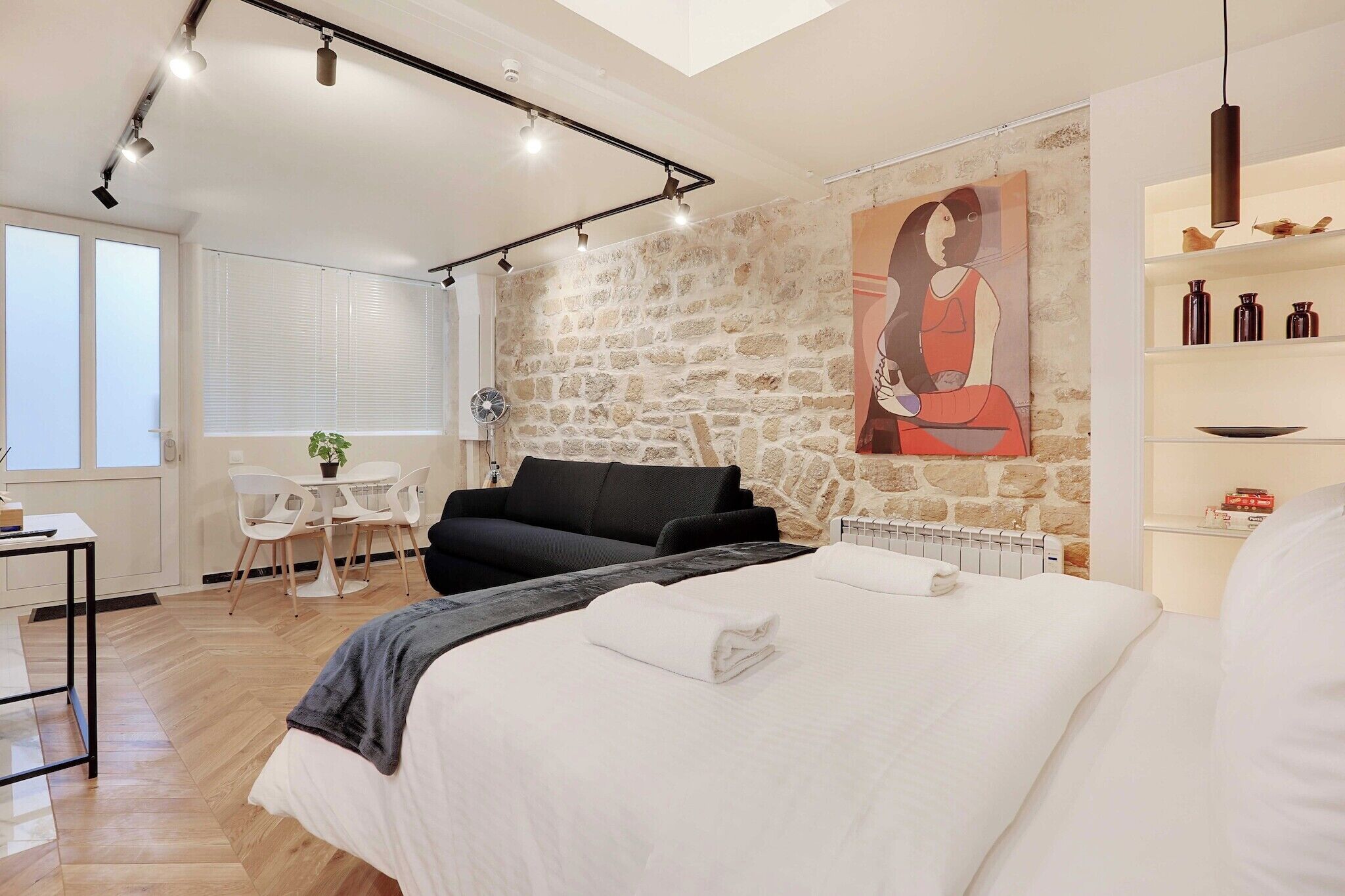 Une chambre moderne avec un grand lit, un canapé noir, un mur en pierre et un tableau.