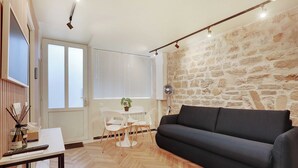 Una sala de estar moderna con una pared de piedra, un sofá negro, una mesa de comedor con sillas y una pequeña mesa con una planta.
