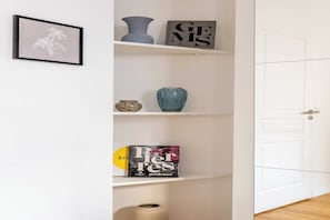 A white door with a handle, a white wall, and a white shelf with various items.