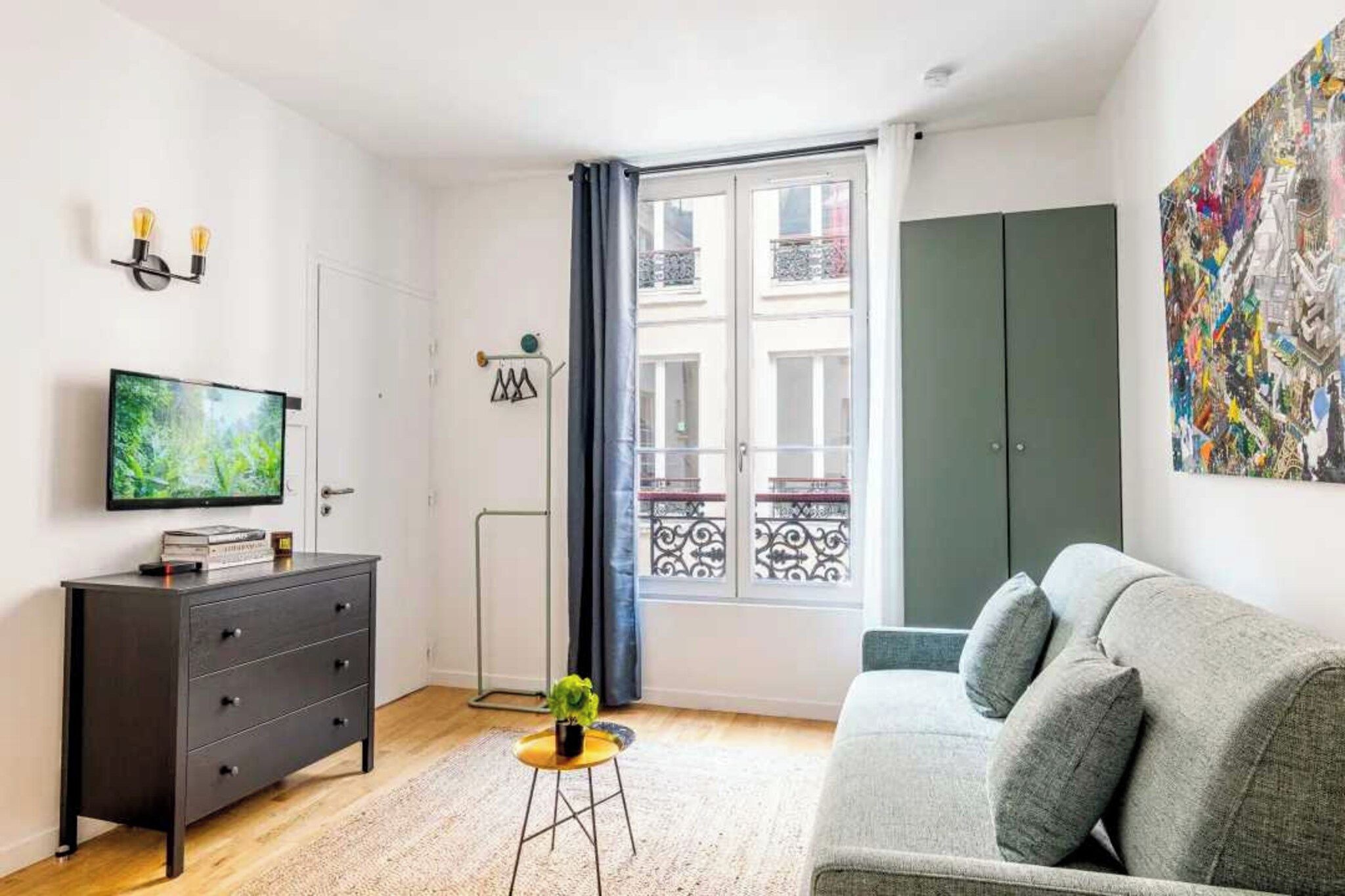 Ein modernes Wohnzimmer mit einem grauen Sofa, einem Fernseher, einem kleinen Tisch mit einer Pflanze und einem Balkon mit Blick.