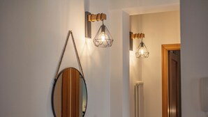 A hallway with a wooden-framed mirror, two wall-mounted pendant lights with geometric designs, and a door leading to another room. - La Finestra sul Mare - Apartment with a view (Gabicce Mare)